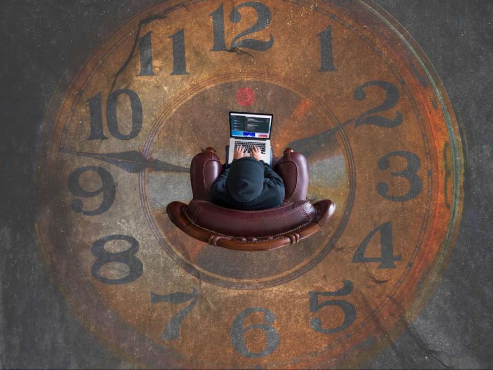 stock image a clock and a person working on a computer 