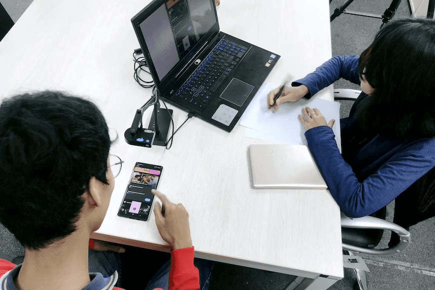 two students working together using a computer and a mobile phone 